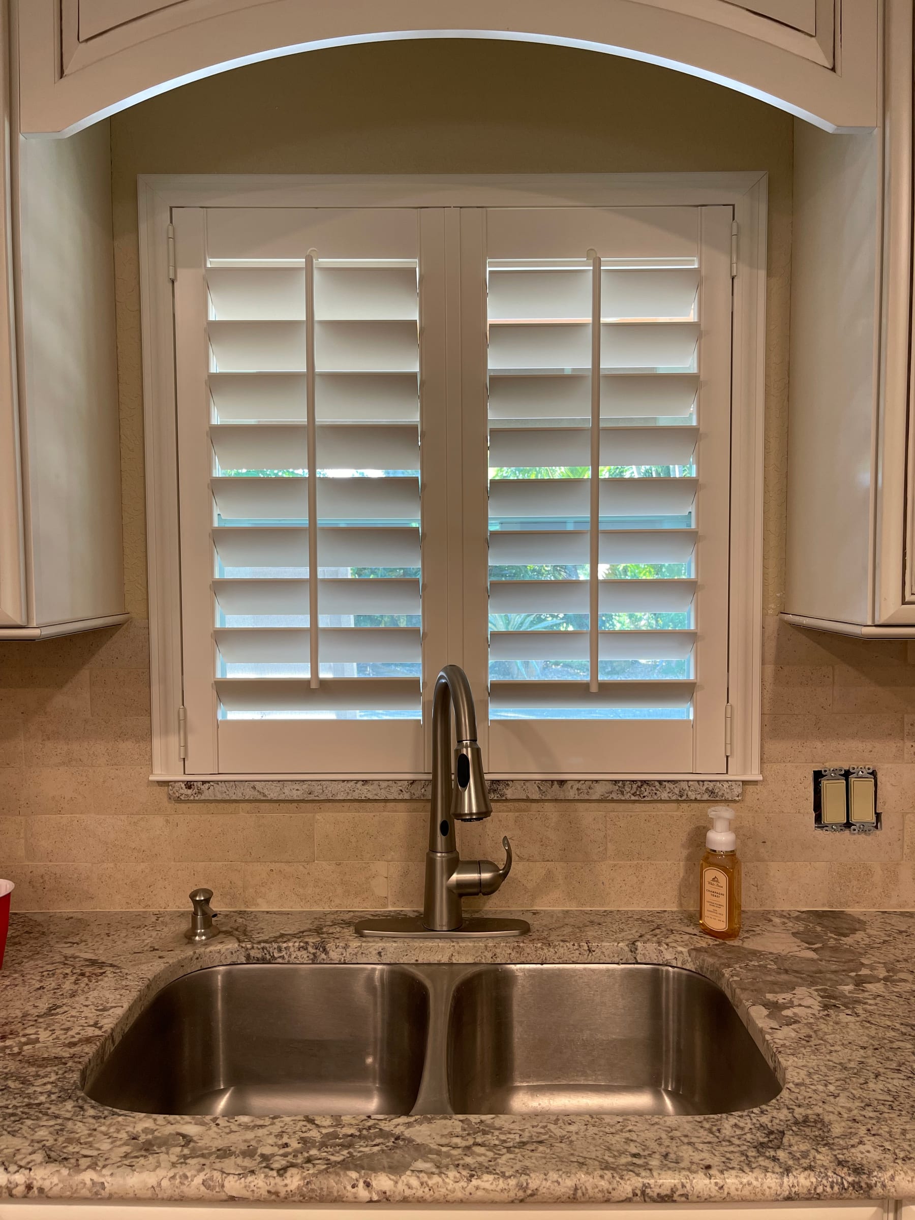 A white shutter with an arched top above a kitchen sink