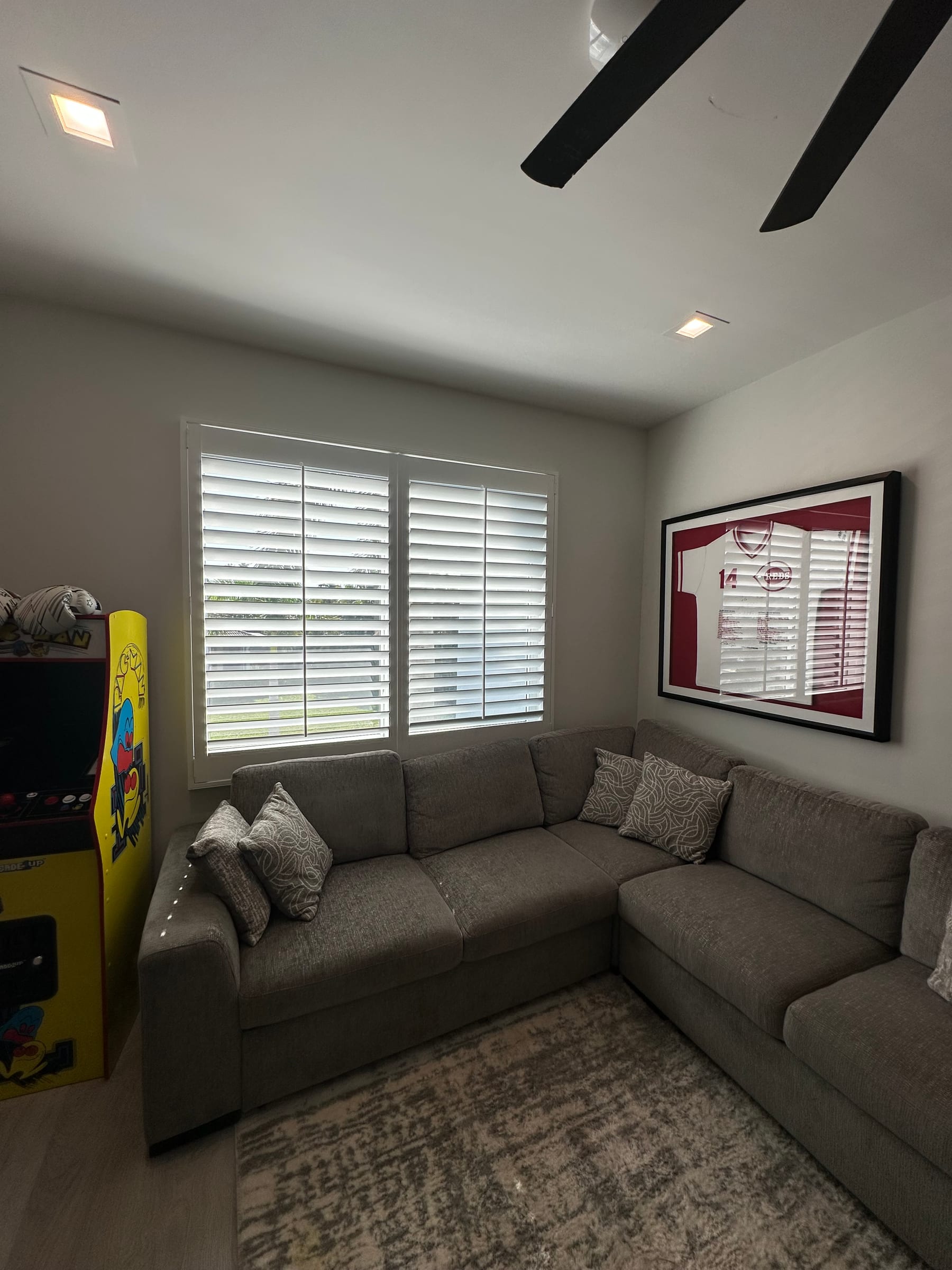 A white shutter on a window beside a corner sofa and a framed print