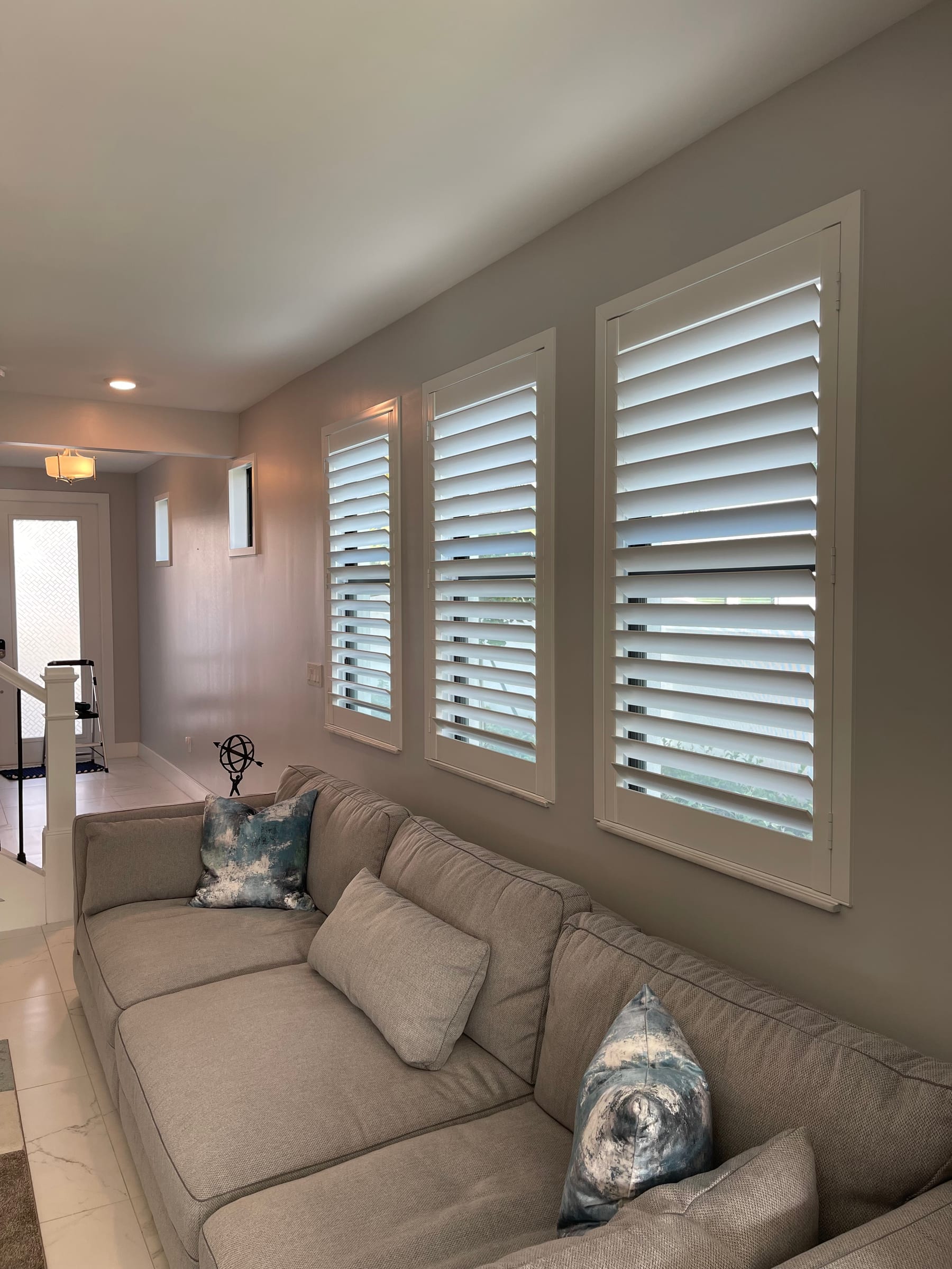 White shutters on tall windows along a living-room wall behind a sofa