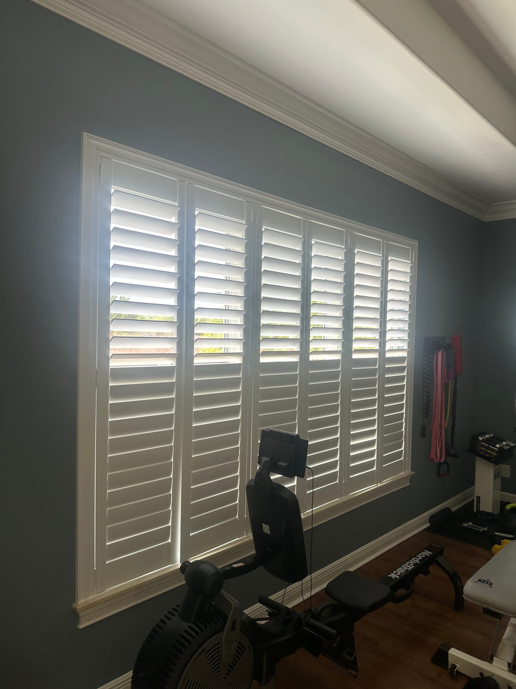 Wide white shutters across a window in a dark-walled exercise room