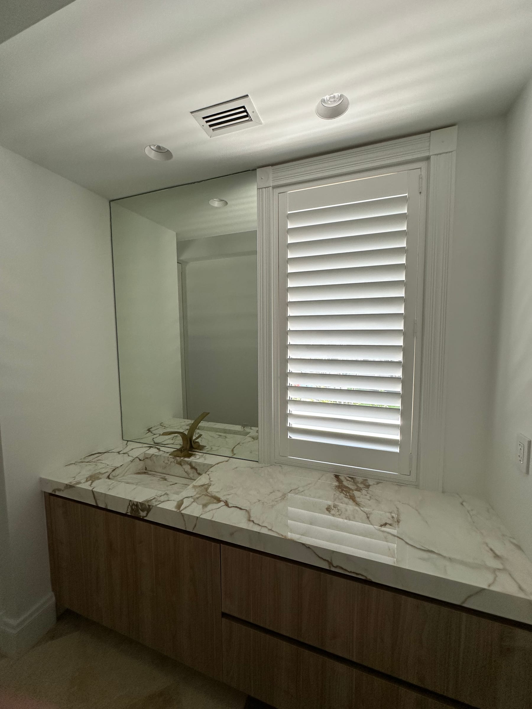 A white shutter beside a marble vanity and a full-width mirror