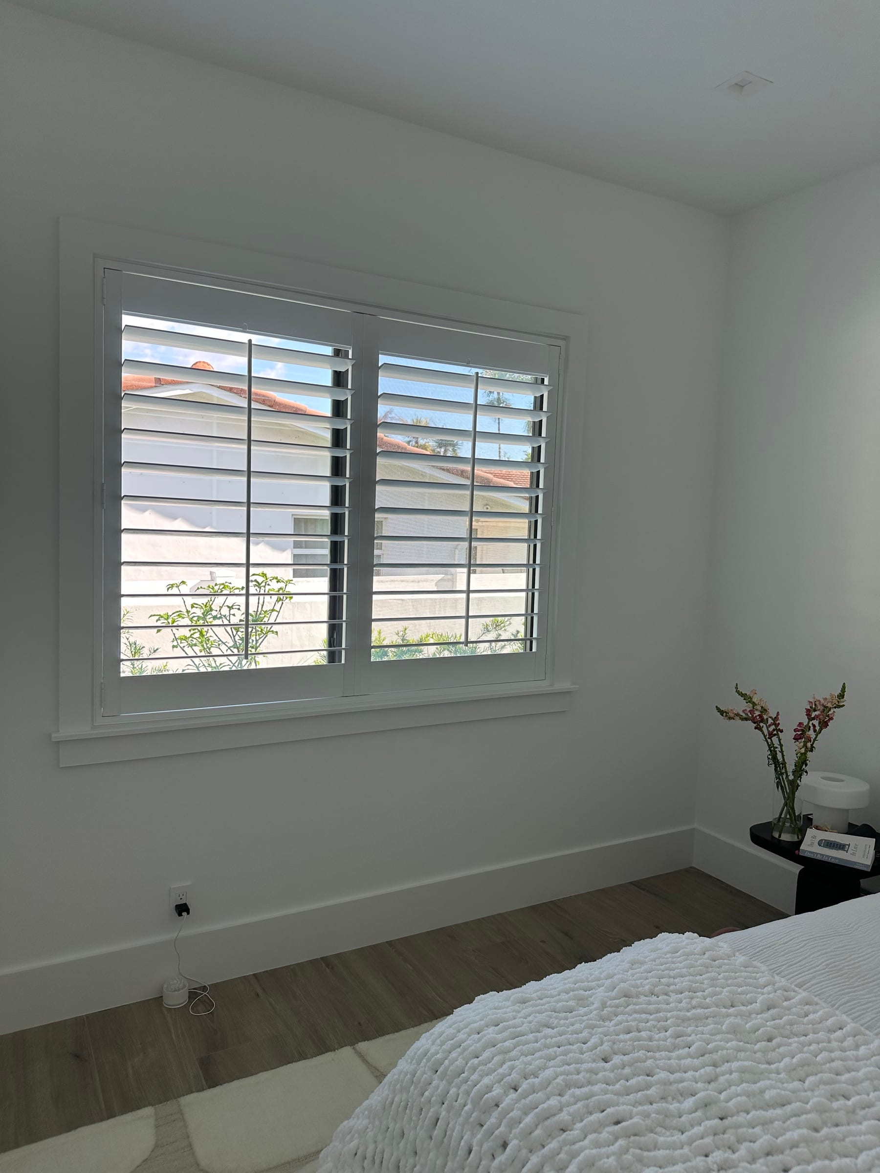 A white shutter on a bedroom window, with a tiled roof beyond the glass